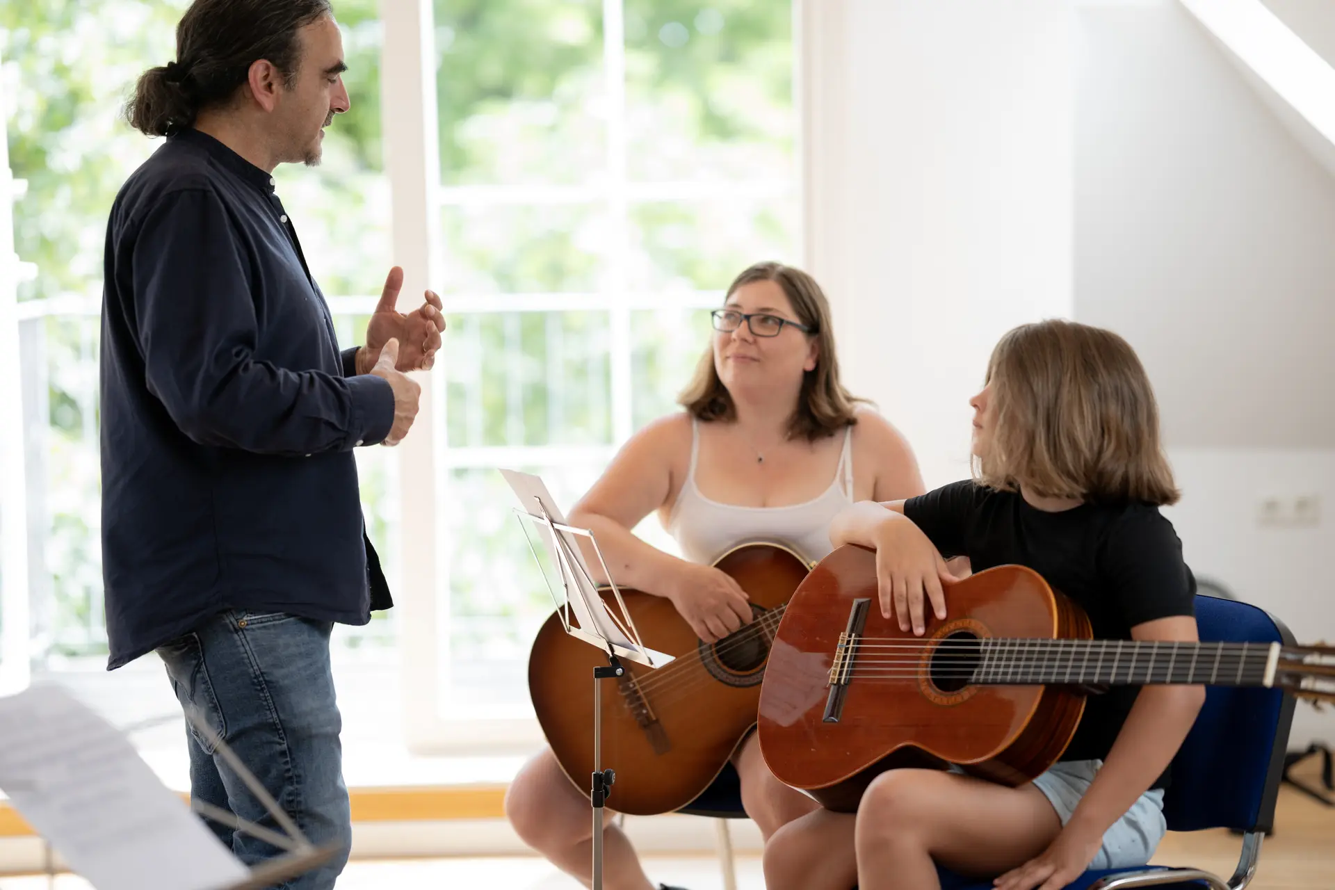 Gitarrenlehrer Dr. Tarek Krohn unterrichtet eine kleine Gruppe mit einer Frau und einem Mädchen