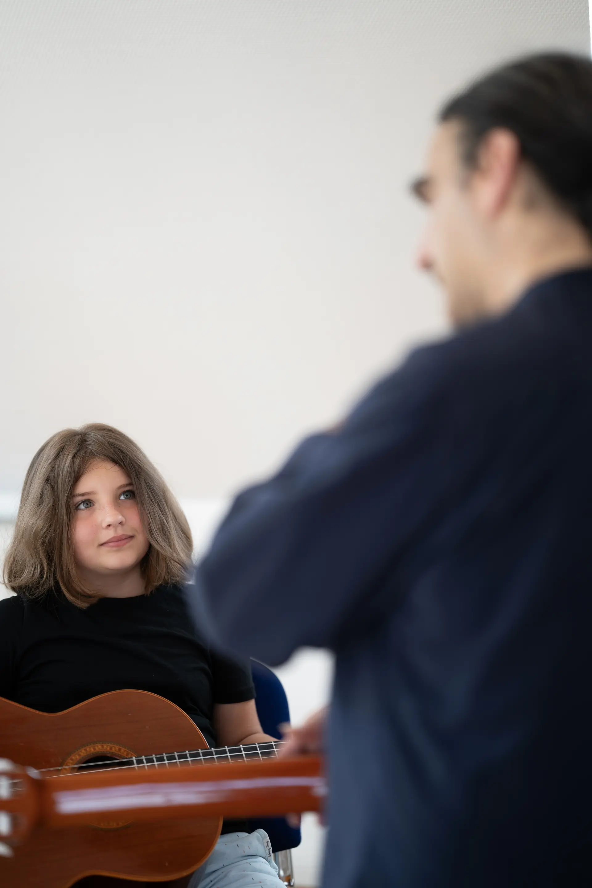 Ein junges Mädchen blickt aufmerksam zu ihrem Gitarrenlehrer im Unterricht
