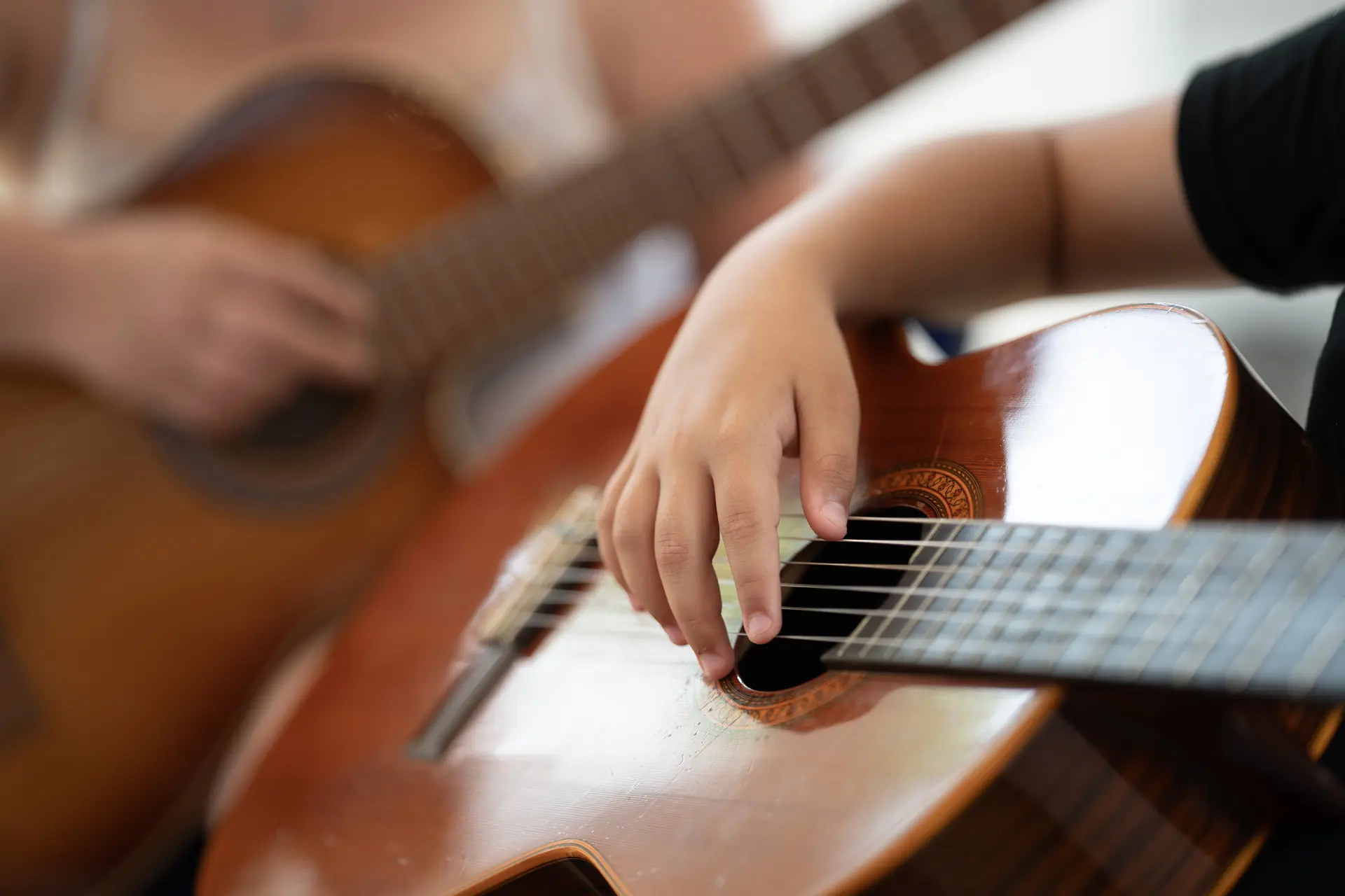 Nahaufnahme der Hände eines Kindes beim Spielen einer klassischen Akustikgitarre