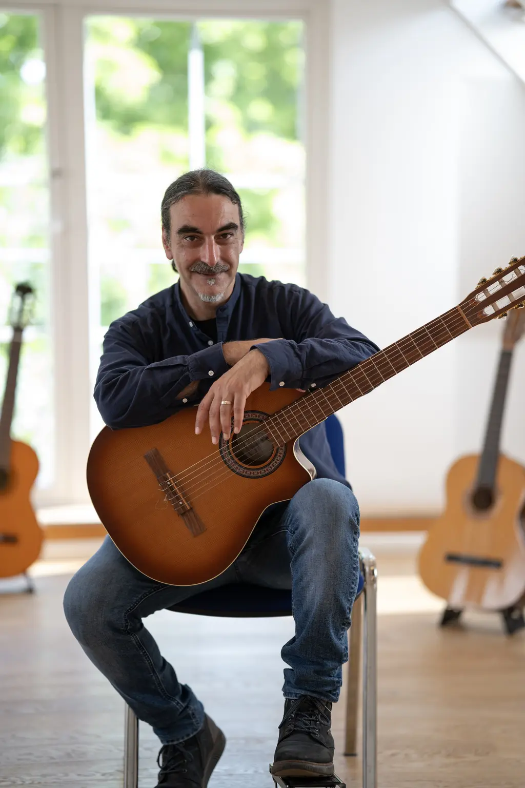 Porträt von Dr. Tarek Krohn mit seiner Akustikgitarre in einem hellen, einladenden Studio