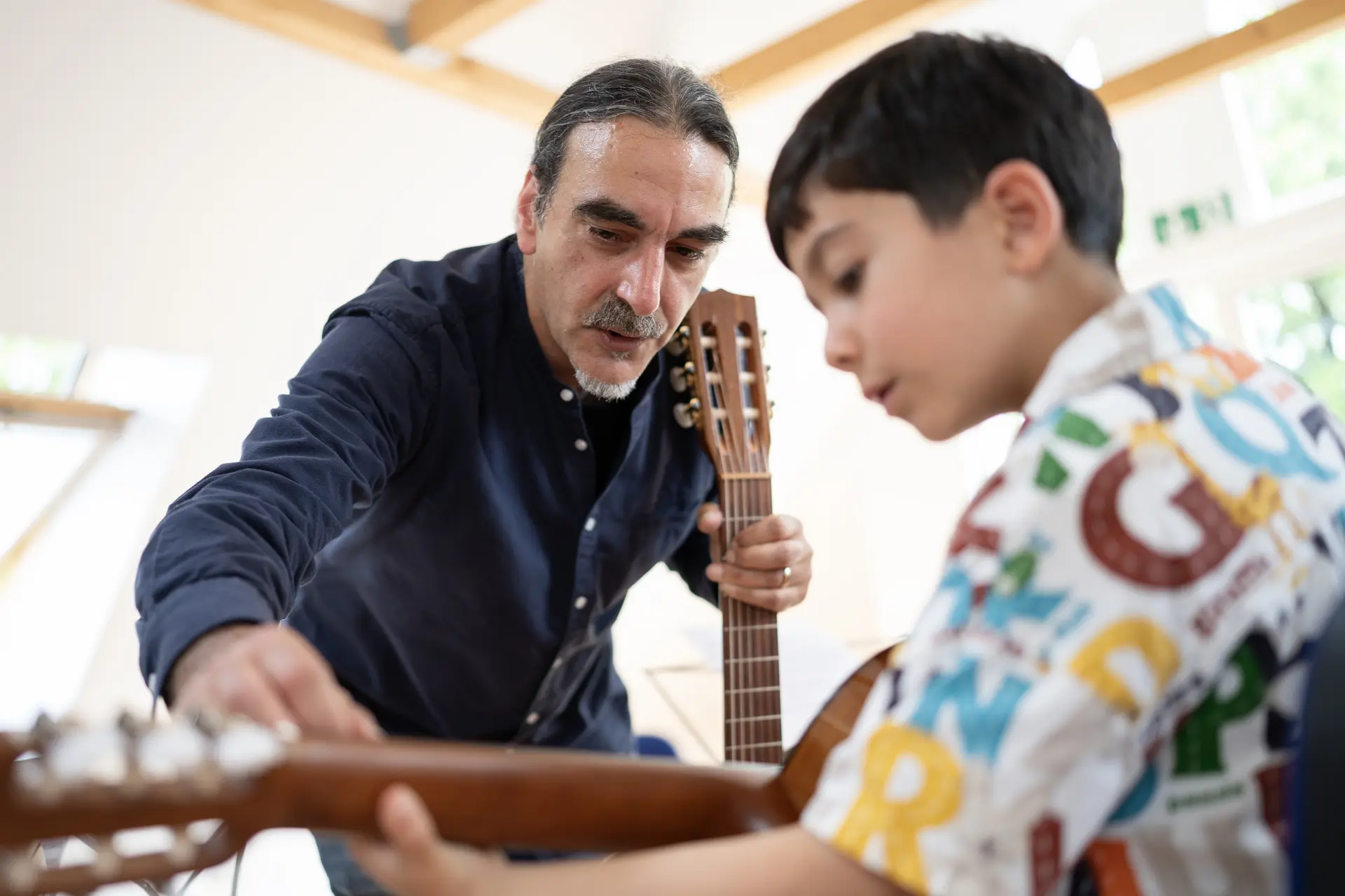 Gitarrenlehrer unterstützt einen Jungen individuell beim Greifen der Gitarrensaiten