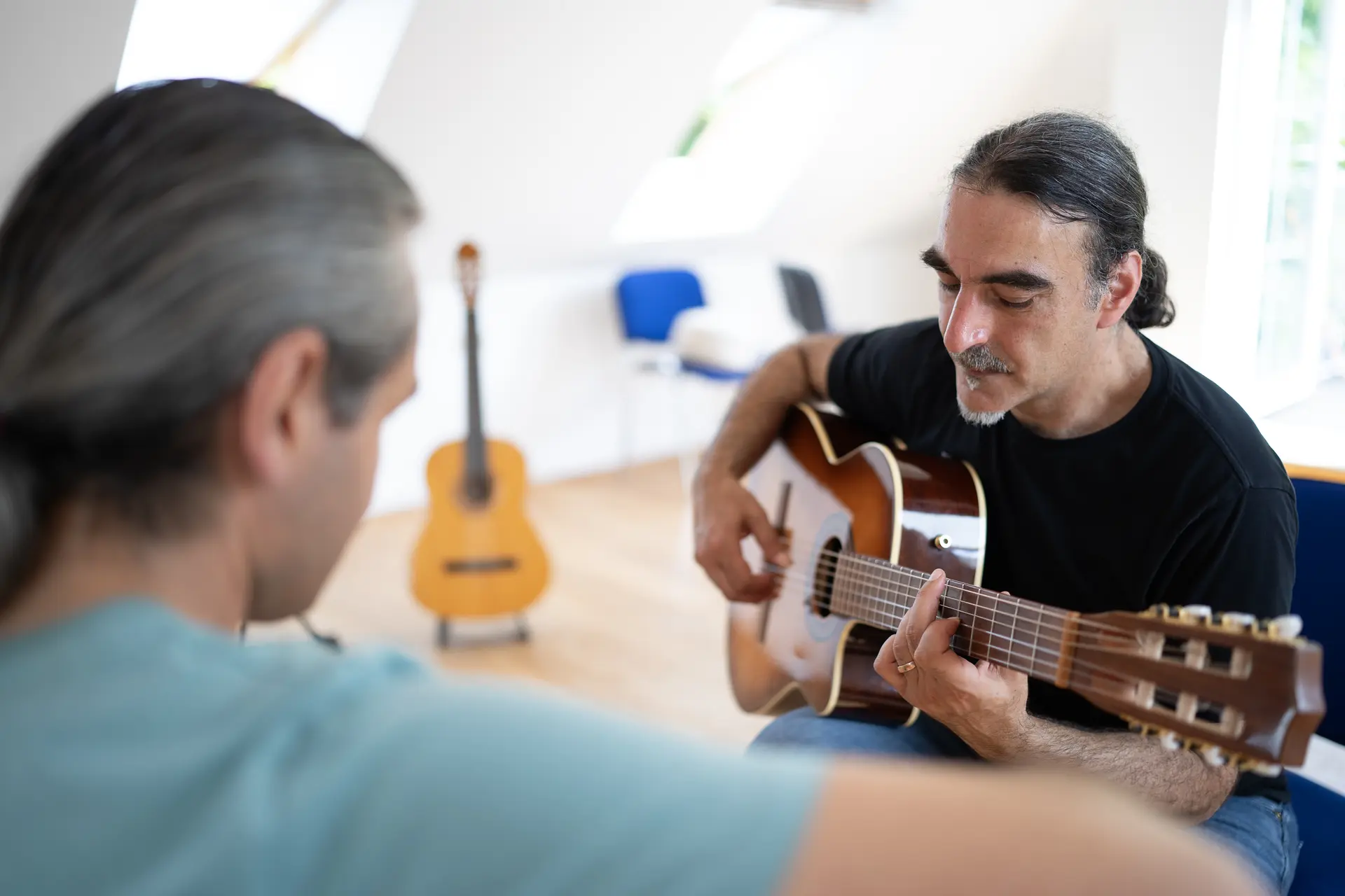 Gitarrenlehrer spielt im Einzelunterricht seinem erwachsenen Schüler auf der Gitarre vor