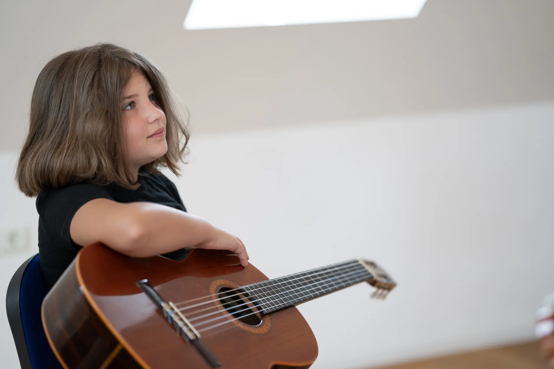 Ein junges Mädchen hält aufmerksam ihre Akustikgitarre während des Gitarrenunterrichts